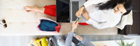 Woman sits on couch with laptop next to man hands her bank card around shopping bagsの写真素材