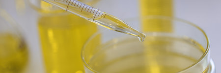 From dispenser for test tube yellow liquid is dripped into glass container next to test tube with liquidsの写真素材