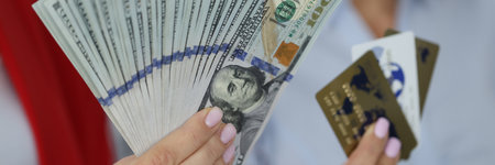 Female hands hold fan of one hundred American dollar bills and credit bank cards.の写真素材