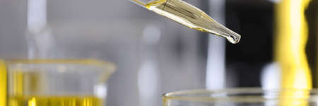 Yellow oil drips from a dispenser into test tube in laboratoryの写真素材