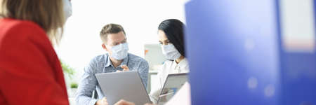 Employees in office are sitting at table wearing protective medical masksの写真素材