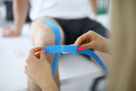 Therapist glueing blue tape on man knee closeupの写真素材