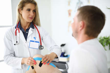 Doctor physiotherapist sticking tapes on man sore kneeの写真素材