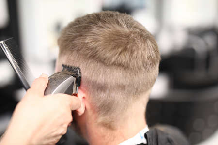 Hairdresser holding hair clipper near man head closeup