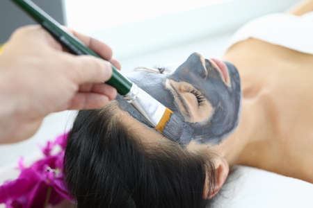 Beautician applying black clay mask to woman with brushの写真素材