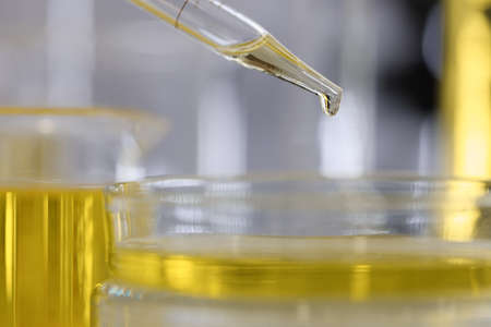 Yellow liquid dripping from pipette into petri dish closeupの写真素材