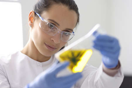 Woman scientists in goggles and gloves holding flask with marijuanaの写真素材