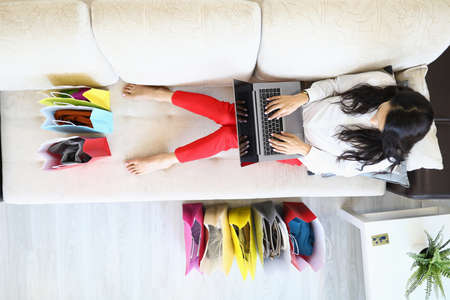 Woman is sitting on couch at home and is shopping online.の写真素材