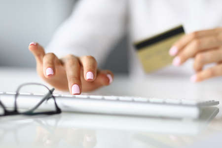 Womans hand holds bank card and fingers on keyboard.