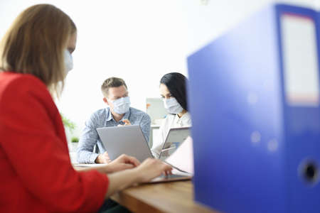 Employees in office are sitting at table wearing protective medical masksの写真素材