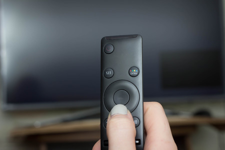 Television remote control changes channels thumb on the blue TV screen displayの写真素材