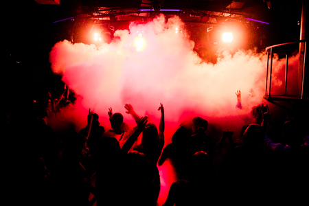 silhouettes of concert crowd in front of bright stage lightsの写真素材