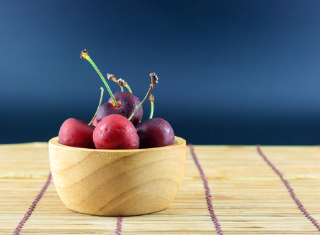 Cherry fruit in wooden bowl on table and black background.