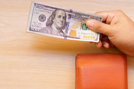 Hand giving money with wallet on wooden table.