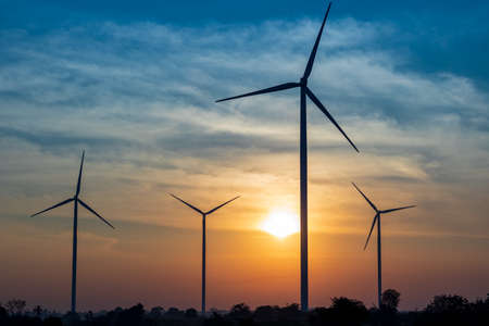 Silhouette of the wind turbine at sunrise on the hill for renewable energy source.