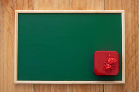 The red square gift box is decorated with red roses on a green chalkboard. Top-view composition.の写真素材