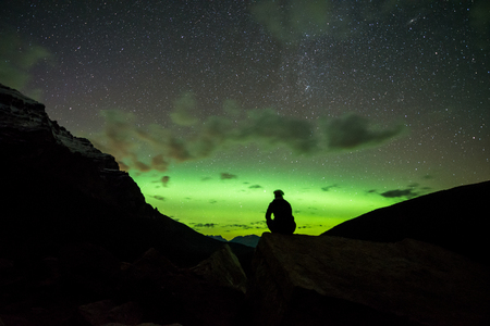 Man sitting on a rock in the mountains watching the Northern Lightsの写真素材
