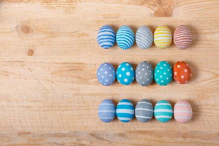 Twelve colorful handmade Easter eggs on a wooden background with space left. Flat lay style