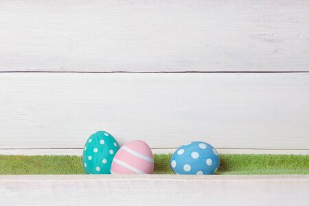 Three colorful handmade easter eggs lie on a green lawn on a white wooden backgroundの写真素材
