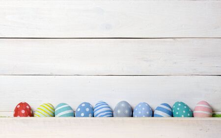 Ten colorful handmade Easter eggs lined up in a row against on white wooden background. Flat lay styleの写真素材