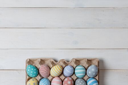 A tray with colorful handmade Easter eggs on white wooden surface with space above. Flat lay style