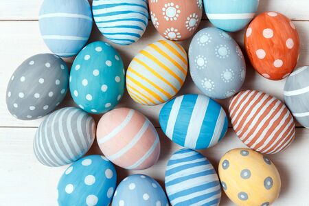 Colorful handmade easter eggs lie on white wooden background. Flat lay style