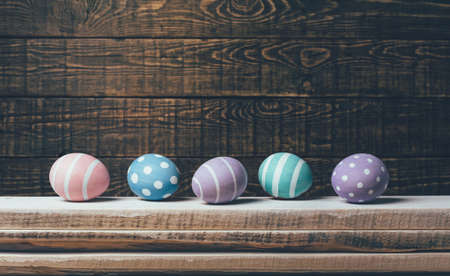 Eight colorful handmade Easter eggs lie in a row on an old wooden background. Flat lay styleの写真素材