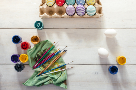 Preparation for Easter. Colorful handmade Easter eggs, paint, brushes on a white wooden background (tabel). Top view. Flat lay styleの写真素材