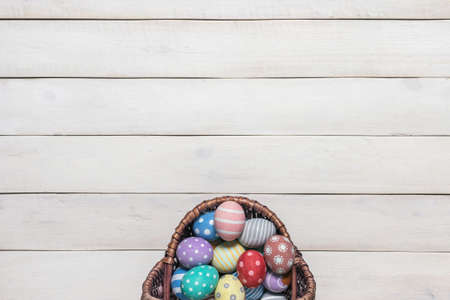 Basket with colorful Easter eggs, painted in handmade on an old white wooden background. Top view, flat lay styleの写真素材