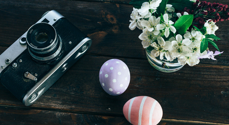 Preparation for Easter. Colorful handmade Easter eggs, paint, retro camera and vase with flowers on a dark wooden backgroundの写真素材