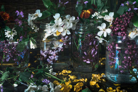 Picturesque bouquets of colorful spring flowers in glass vases bottles on a dark wooden background table. Close upの写真素材