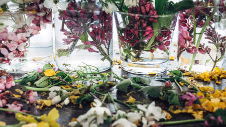 Picturesque bouquets of colorful spring flowers in glass vases bottles, standing in a row on a light wooden background table.の写真素材