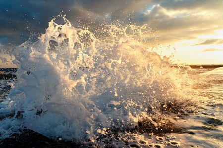 A large wave breaks about a breakwater close-up against a sunset background. Seascapeの写真素材