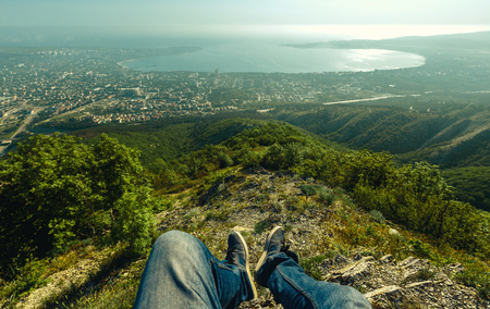 Pair of legs with shoes against the backdrop of the picturesque landscape of the city and the sea on sunny day. First person photo. Concept of travel, adventure and discoveryの写真素材