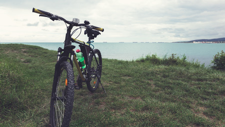 A bicycle stands on a green lawn of the sea with a view of the mountain rangeの写真素材