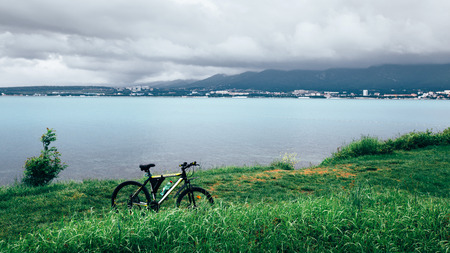 A bicycle stands on a green lawn of the sea coast with a view of the mountain range concept of active recreation and healthy lifestyleの写真素材