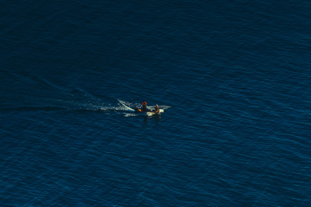 Lonely boat sails along beautiful blue surface of the sea, concept of moving forward and overcoming difficultiesの写真素材
