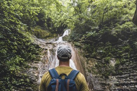 Traveler Has Reached Destination, Enjoying View Of Waterfall And Beauty The Unspoilt Nature. Contemplation Adventure Conceptの写真素材