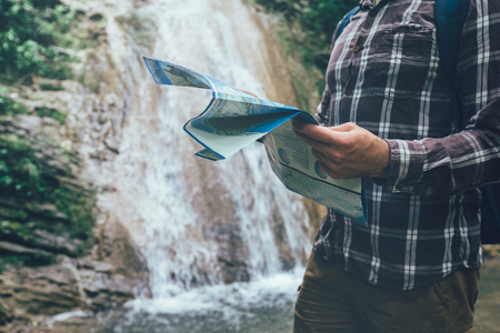 Unrecognizable Young Traveler With Backpack Is Standing By Waterfall And Looks At The Map Holidays And Tourism Conceptの写真素材