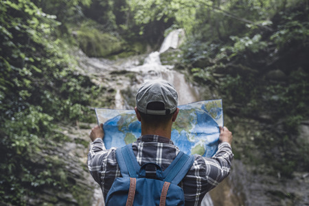 Hiker With Backpack Standing By The Waterfall And Looks At  Map Rear View Holidays And Tourism Conceptの写真素材