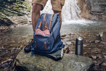 Hiker Man Feet, Backpack And Thermos On Waterfall Background Adventure Hiking Travel Conceptの写真素材