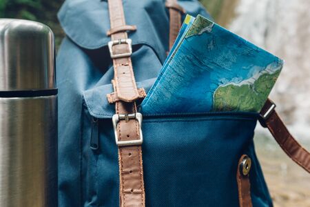 Hipster Blue Backpack, Map And beverage containers Closeup. View From Front Tourist Traveler Bag On Waterfall Background. Journey Adventure Hiking Conceptの写真素材