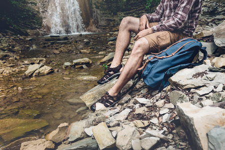 Unrecognizable Traveler With Backpack Sits On The River And Enjoys Surrounding View Exploring Adventure Hiking Conceptの写真素材