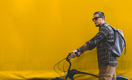 Handsome Adult Man In Sunglasses Walks With A Bicycle Along A Yellow Wall Copy Spaceの写真素材