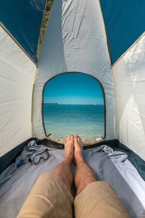 Tourist Man Lying In Tent With A View Of  Sea Summer Beach Holiday Vacation Concept. View Of Legs. Point Of View Shotの写真素材