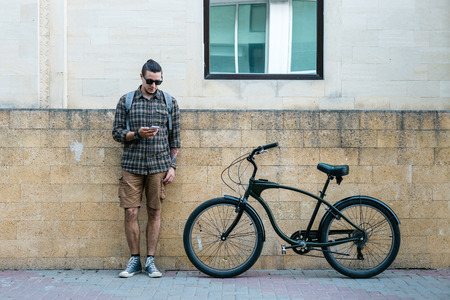 Handsome Young Man Cyclist Standing Next To Bike And His Looking At Smartphone. Street Lifestyle Urban Everyday Conceptの写真素材