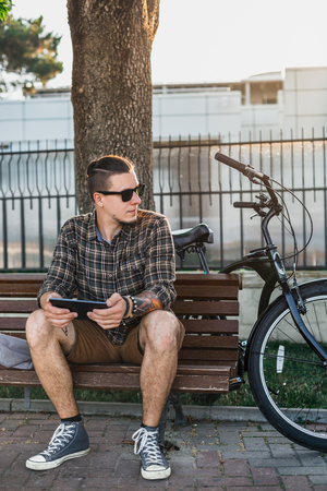 Young Man Cyclist Resting On Bench In Summer Park And Using Tablet Communication Connection Digital Devices Technology Conceptの写真素材