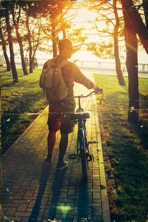Handsome Young Man Walking With Bike In Summer Park At Sunset, Rear View Holiday Weekend Activityの写真素材