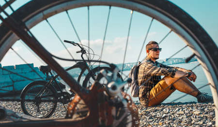 Handsome Male Cyclist Sits On Seashore And Looking At Sea View. Holiday Travel Activity Concept