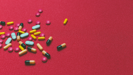 Different Colorful Pills, Tablets And Capsules On Red Backgroundの写真素材